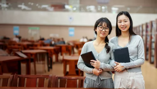 Two students holding books in a library